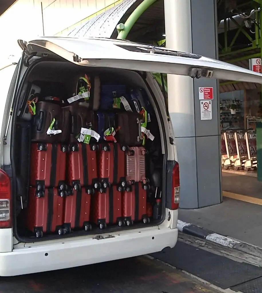 1 Hiace putih sedang memuat koper merah.